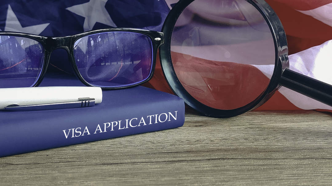 Magnifying glass and glasses on a book titled “VISA APPLICATION”